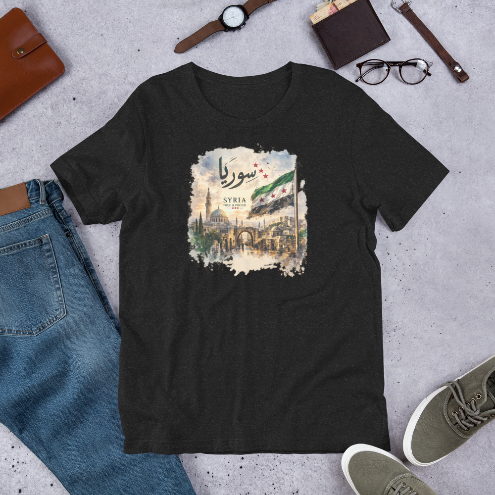 Mockup of a unisex graphic T-shirt featuring a vintage-style Syria-inspired artwork with Arabic calligraphy, historic architecture, scenic landscape, and the Syrian flag.